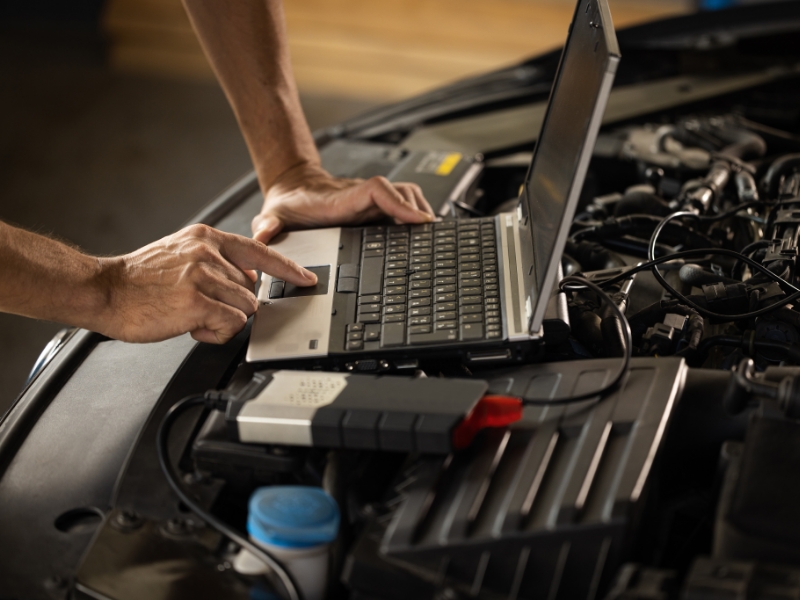 Technician using laptop for car engine diagnostics