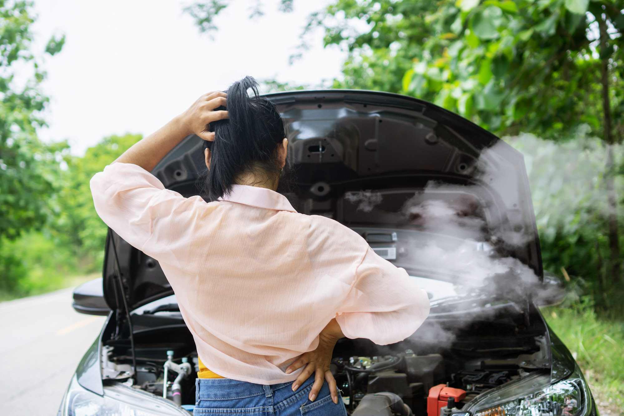 Woman examining smoking car engine on roadside
