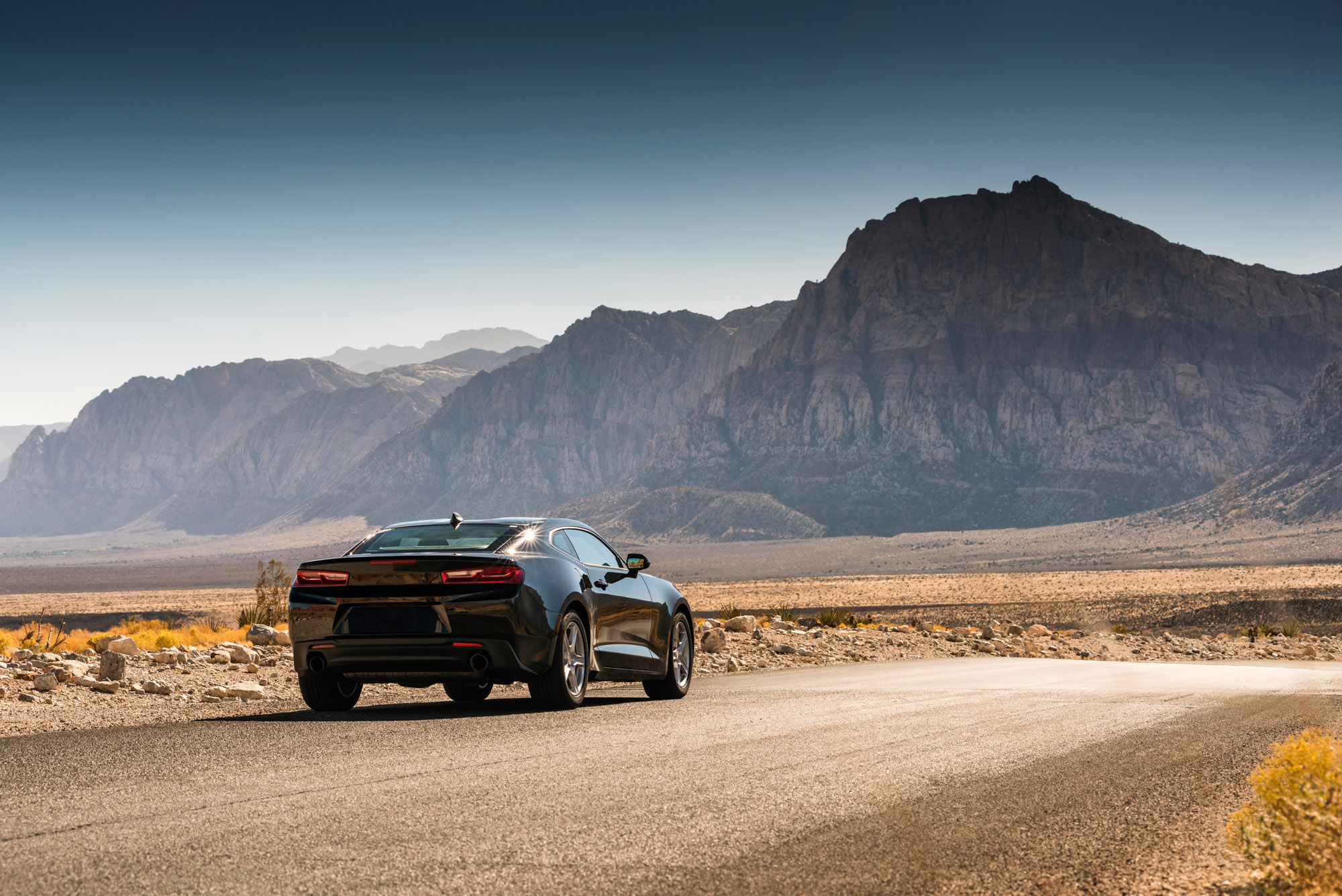 Black sports car on desert road by mountains