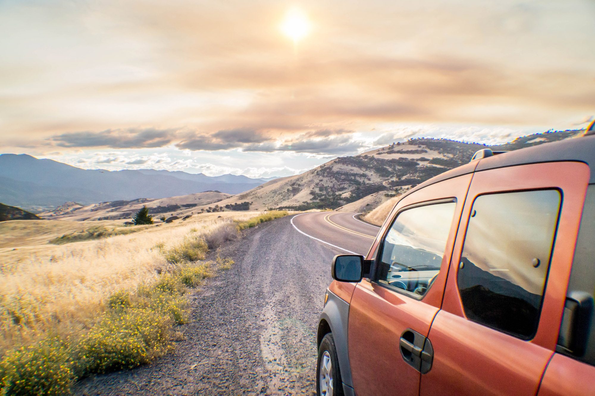 Orange SUV driving on winding mountain road at sunset