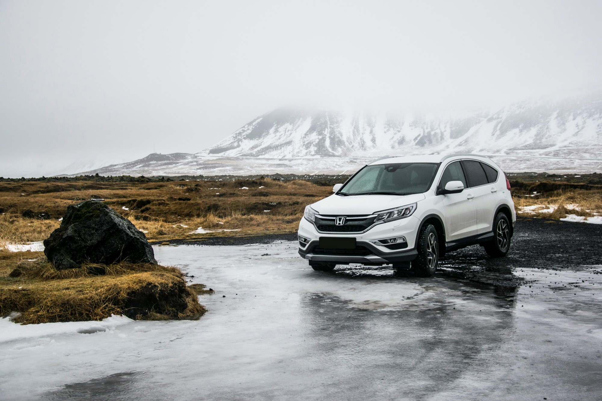 White SUV on icy road by snowy mountains