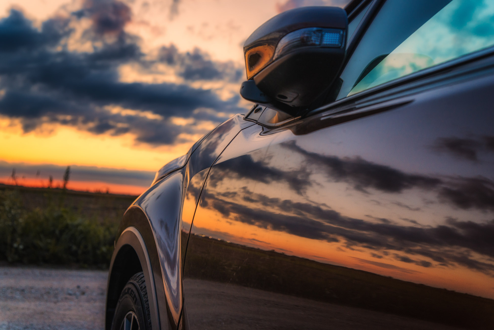 Car side mirror reflecting sunset sky
