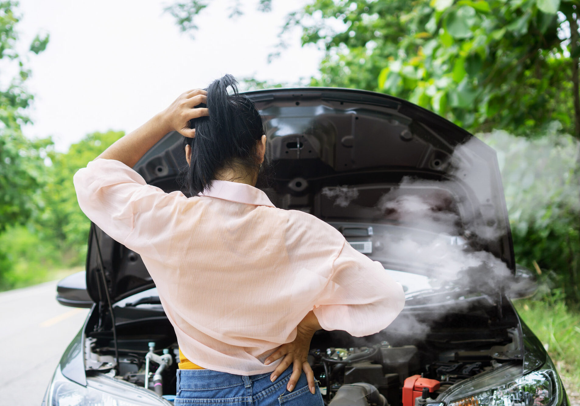 Woman examining smoking car engine on roadside